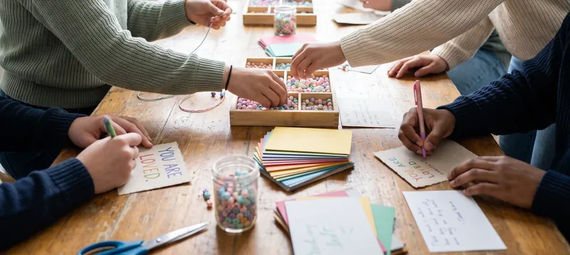 Volunteers at a long table making beaded bracelets and writing encouragement cards